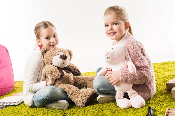 Щасливі маленькі сестри грають з м'якими іграшками разом, сидячи на підлозі ізольовані на білому — стокове фото