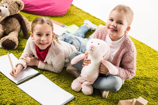 Hermanas pequeñas dibujando y jugando con juguetes en el suelo - foto de stock