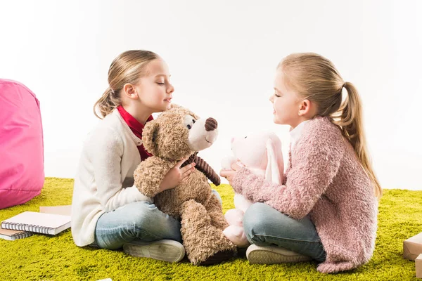 Hermanas pequeñas jugando con juguetes suaves mientras están sentadas en el suelo aisladas en blanco - foto de stock