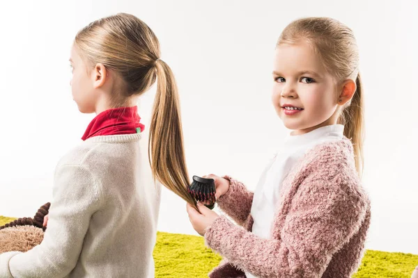 Beautiful child brushing hair of sister while sitting on floor isolated on white — Stock Photo