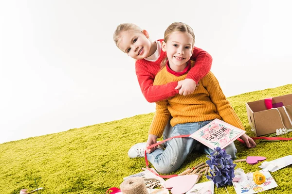 Little sisters sitting on floor while making mothers day greeting card and embracing isolated on white — Stock Photo