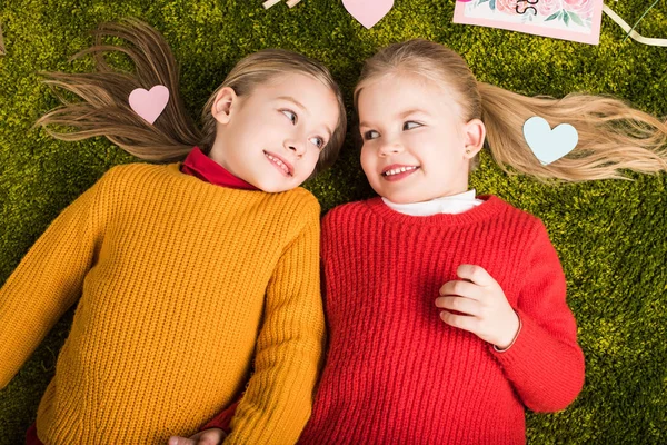 Vista dall'alto di adorabili sorelline sdraiate su un tappeto circondato da cuori — Foto stock