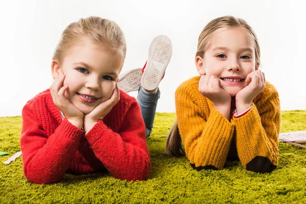 Adorables hermanas pequeñas aisladas tumbadas en la alfombra verde y mirando a la cámara aislada en blanco - foto de stock