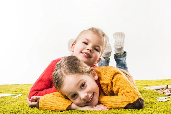 Happy little sisters isolated lying on green carpet and looking at camera isolated on white — Stock Photo