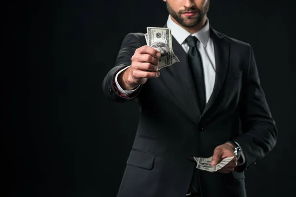Vista recortada de hombre de negocios en chaqueta con billetes de dólar, aislado en negro - foto de stock