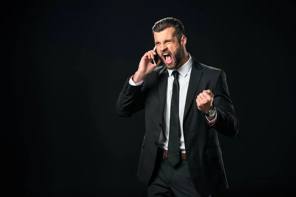 Exitoso hombre de negocios gritando mientras habla en el teléfono inteligente, aislado en negro — Stock Photo