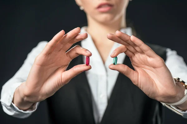 Vista recortada de la mujer de negocios sosteniendo píldoras azules y rojas, aislado en negro - foto de stock