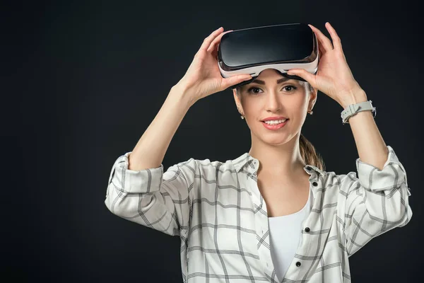 Mujer sonriente usando auriculares de realidad virtual, aislados en negro - foto de stock