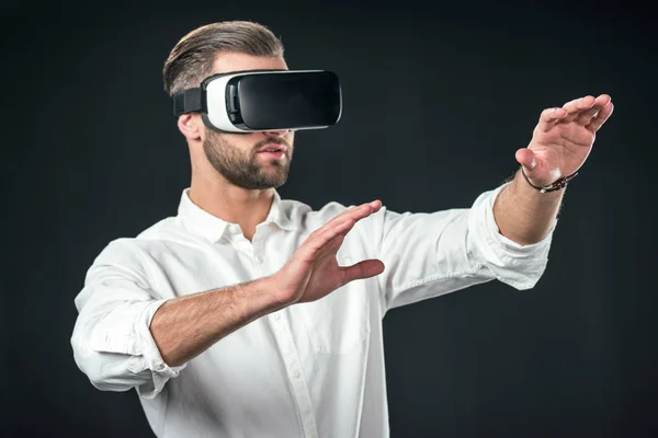 Homem gesticulando e usando fone de ouvido realidade virtual, isolado em preto — Fotografia de Stock