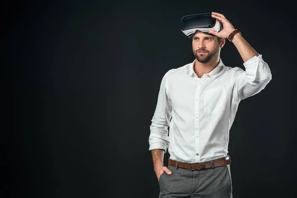 Hombre guapo usando auriculares de realidad virtual, aislado en negro - foto de stock