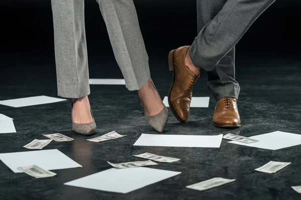 Vista recortada de los empresarios de pie en el suelo con documentos y billetes de dólar, en negro - foto de stock