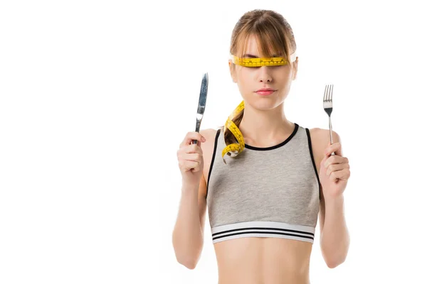 Slim woman with measuring tape tied around her eyes holding fork and knife isolated on white — Stock Photo