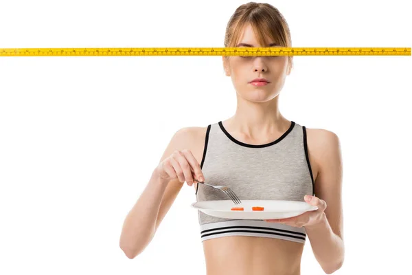 Slim woman eating cherry tomato with measuring tape in front her eyes isolated on white — Stock Photo