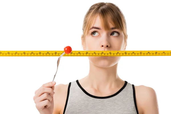 Young woman with measuring tape in front her mouth trying to eat fresh tomato isolated on white — Stock Photo