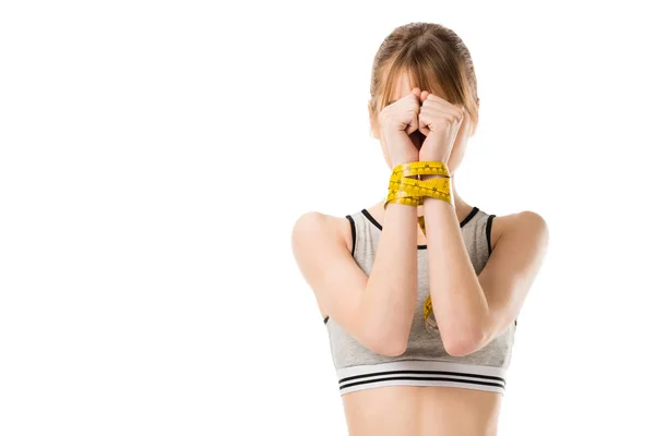 Attractive slim woman covering face with hands tied in measuring tape isolated on white — Stock Photo