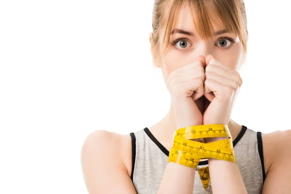 Mujer joven asustada cubriendo la cara con las manos atadas en cinta métrica aislada en blanco - foto de stock