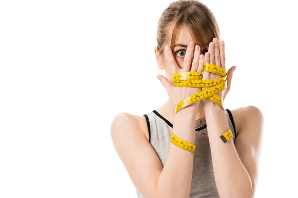 Frightened young woman covering face with hands tied in measuring tape isolated on white — Stock Photo