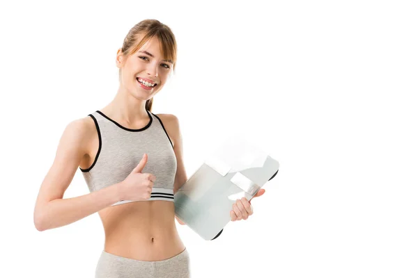 Smiling slim woman holding scales and showing thumb up isolated on white — Stock Photo