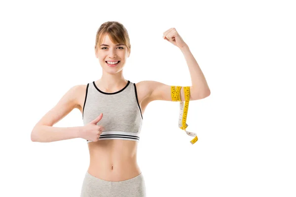 Joven mujer delgada mostrando sus bíceps atados con cinta métrica y el pulgar hacia arriba aislado en blanco - foto de stock