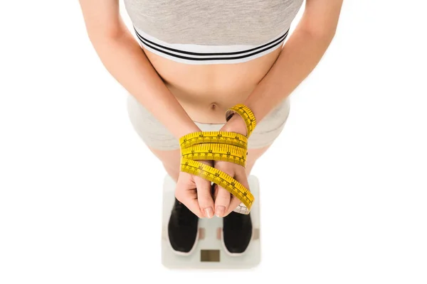 Cropped shot of young woman with hands tied with measuring tape standing on scales isolated on white — Stock Photo