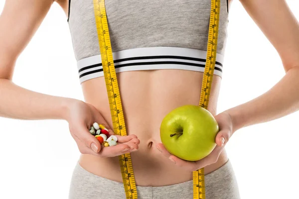 Tiro recortado de mujer delgada sosteniendo manzana fresca y pastillas aisladas en blanco - foto de stock