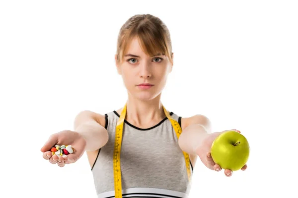 Joven mujer delgada sosteniendo manzana fresca y pastillas aisladas en blanco - foto de stock