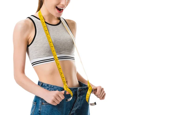 Happy young slim woman with measuring tape in oversized jeans isolated on white — Stock Photo