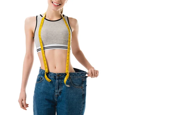 Smiling slim woman with measuring tape in oversized jeans isolated on white — Stock Photo