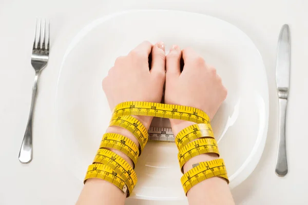 Cropped shot of woman with hands tied with measuring tape lying on plate — Stock Photo