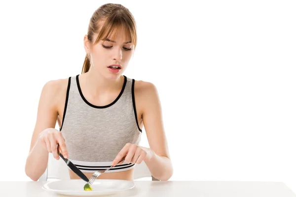 Disgusted slim woman eating piece of broccoli from plate isolated on white — Stock Photo