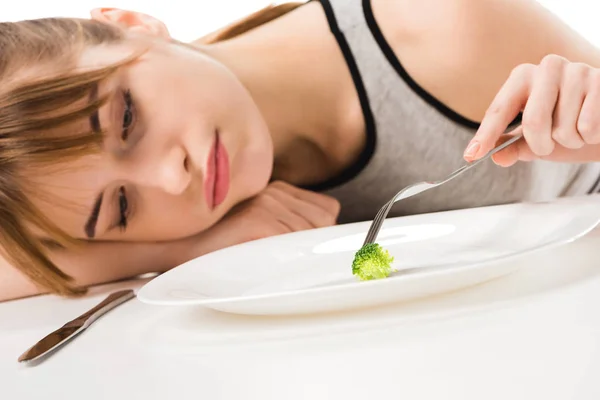 Depressed slim woman eating piece of broccoli from plate isolated on white — Stock Photo