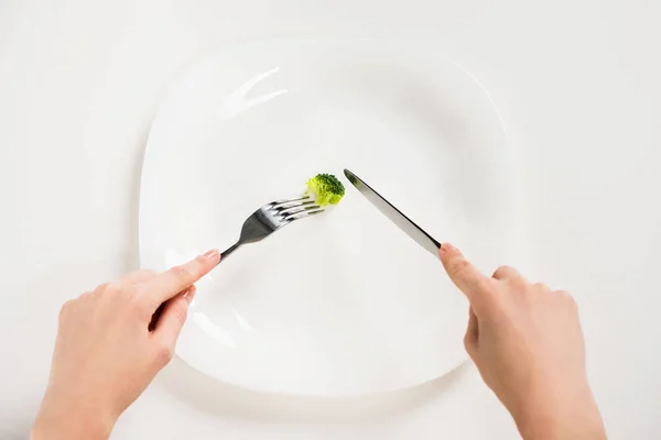 Cropped shot of woman eating small piece of broccoli with fork and knife — Stock Photo