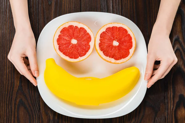 Abgeschnittene Aufnahme einer Frau, die einen Teller mit halbierter Grapefruit und Bananenkoffer hält — Stockfoto