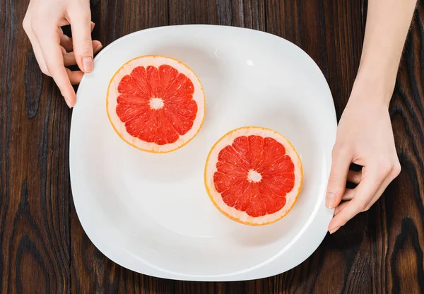 Tiro cortado de mulher segurando placa com toranja reduzida pela metade — Fotografia de Stock