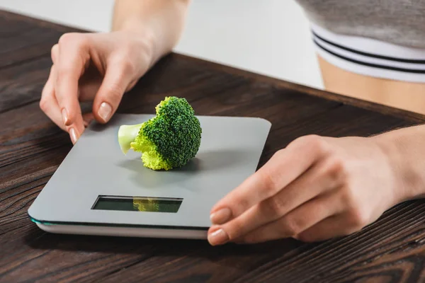 Cropped shot of woman measuring weight of broccoli — Stock Photo