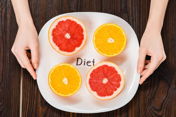 Cropped shot of woman holding plate with halved citrus fruits and diet inscription — Stock Photo