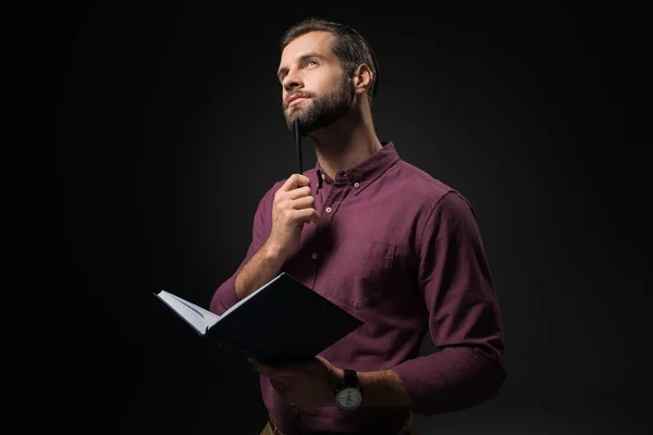 Retrato de empresario pensativo con cuaderno aislado en negro - foto de stock