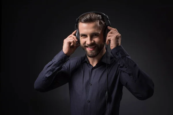 Portrait d'un homme souriant écoutant de la musique dans des écouteurs isolés sur noir — Photo de stock