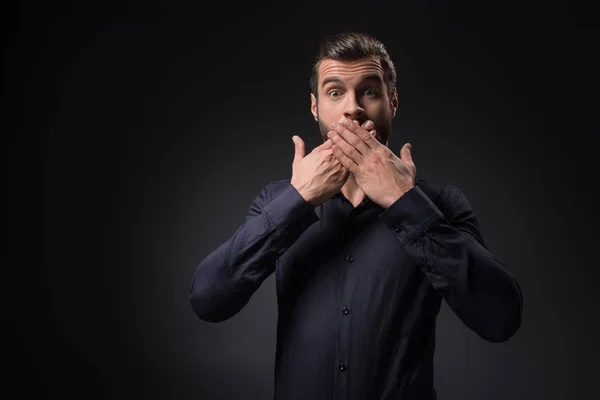 Retrato del hombre sorprendido cubriendo la boca con las manos aisladas en negro - foto de stock