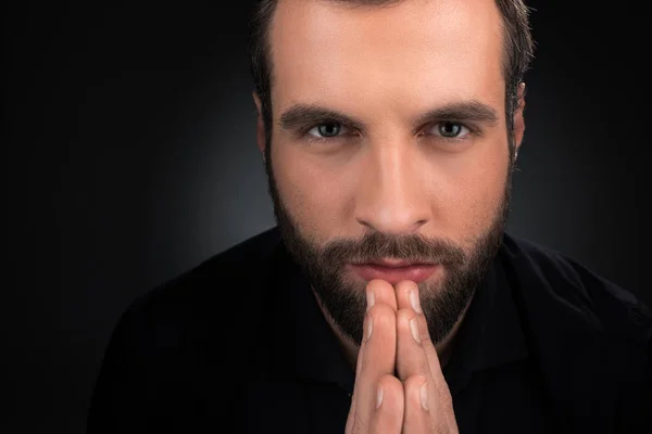 Portrait of man looking at camera while praying isolated on black — Stock Photo