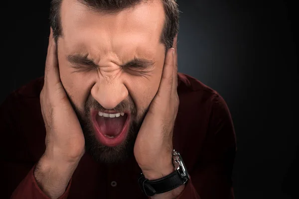 Retrato del hombre gritando cubriendo las orejas aisladas en negro — Stock Photo