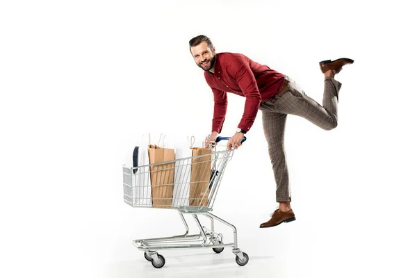 Hombre sonriente con carrito lleno de bolsas de compras y chaqueta aislada en blanco - foto de stock
