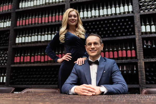 Equipo de gerentes de restaurantes adultos sonrientes mirando la cámara frente a los estantes de almacenamiento de vino - foto de stock