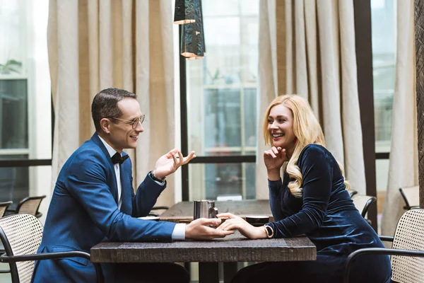 Side view of happy adult couple having date at restaurant and holding hands — Stock Photo