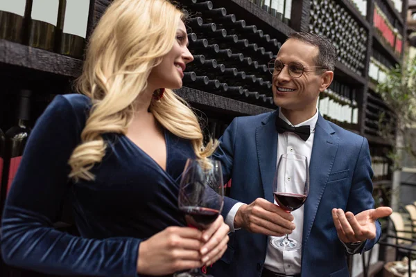 Приваблива доросла пара п'є вино перед полицями для зберігання вина — стокове фото