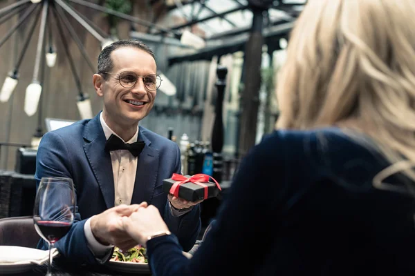 Schöner glücklicher Mann überreicht Valentinstag-Geschenk an Freundin im Restaurant — Stockfoto