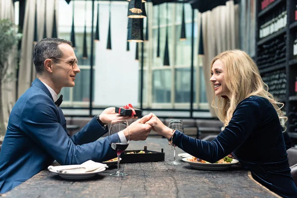 Side view of man presenting valentines day gift to girlfriend at restaurant — Stock Photo