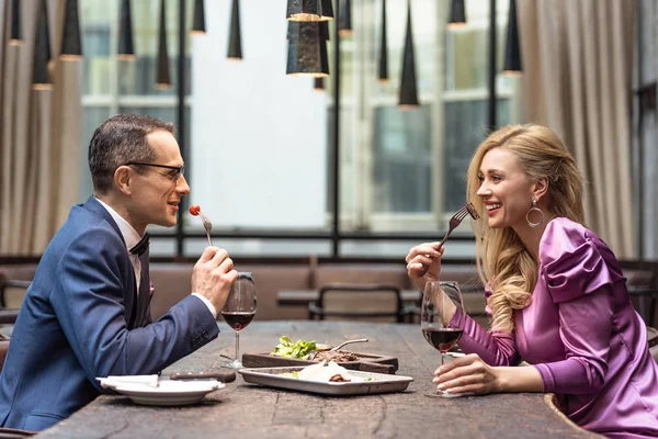 Vista lateral de una hermosa pareja adulta comiendo en un restaurante de lujo - foto de stock