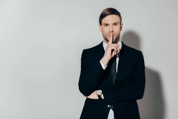 Young confident businessman in suit showing silence gesture on white background — Stock Photo