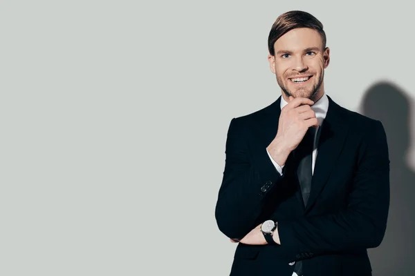 Junger lächelnder Geschäftsmann im Anzug mit Hand am Kinn auf weißem Hintergrund — Stockfoto